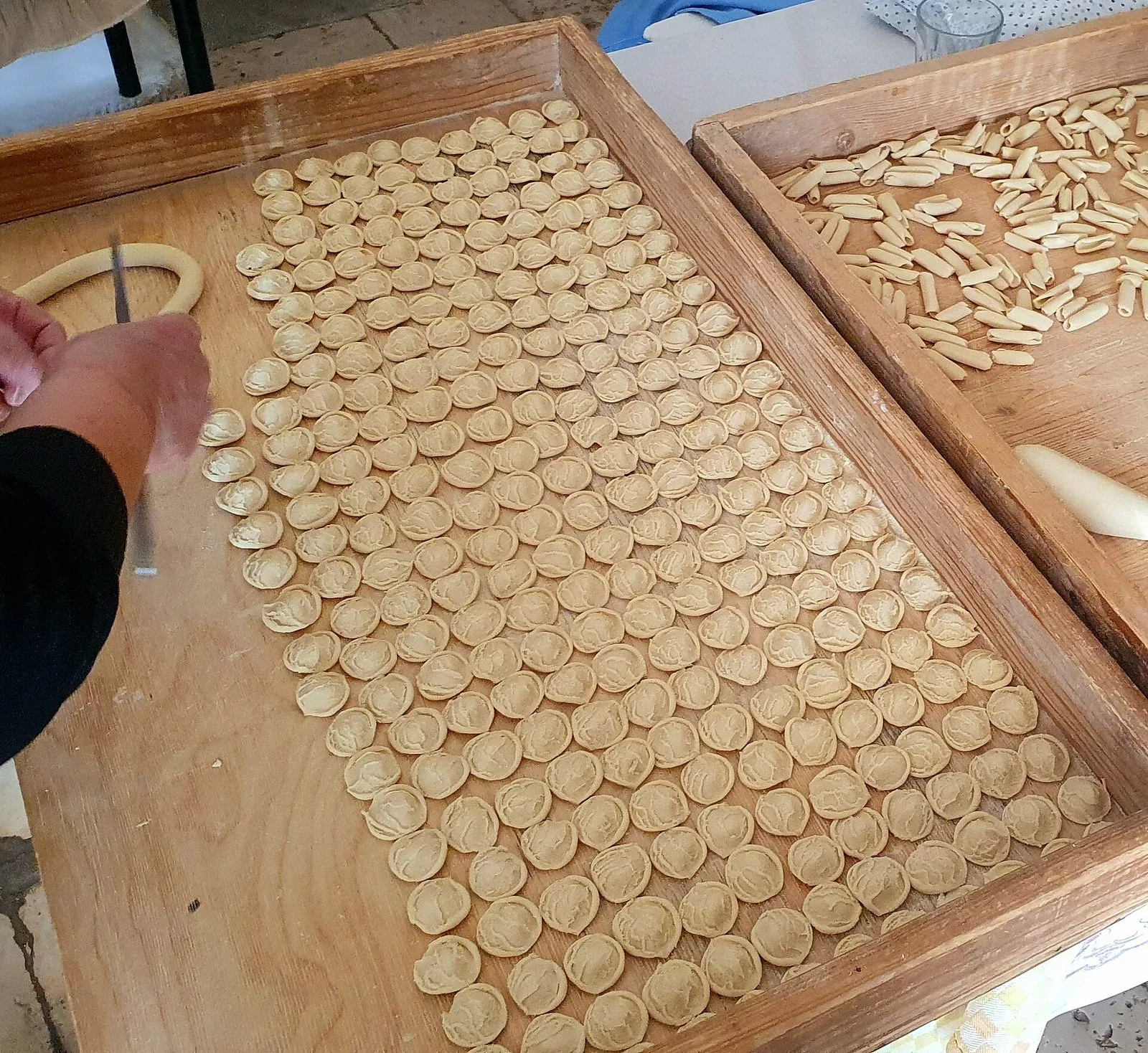 Orecchiette e cavatelli fatti a mano disposti ad asciugare su due grandi tavolieri di legno, con una mano che lavora l'impasto